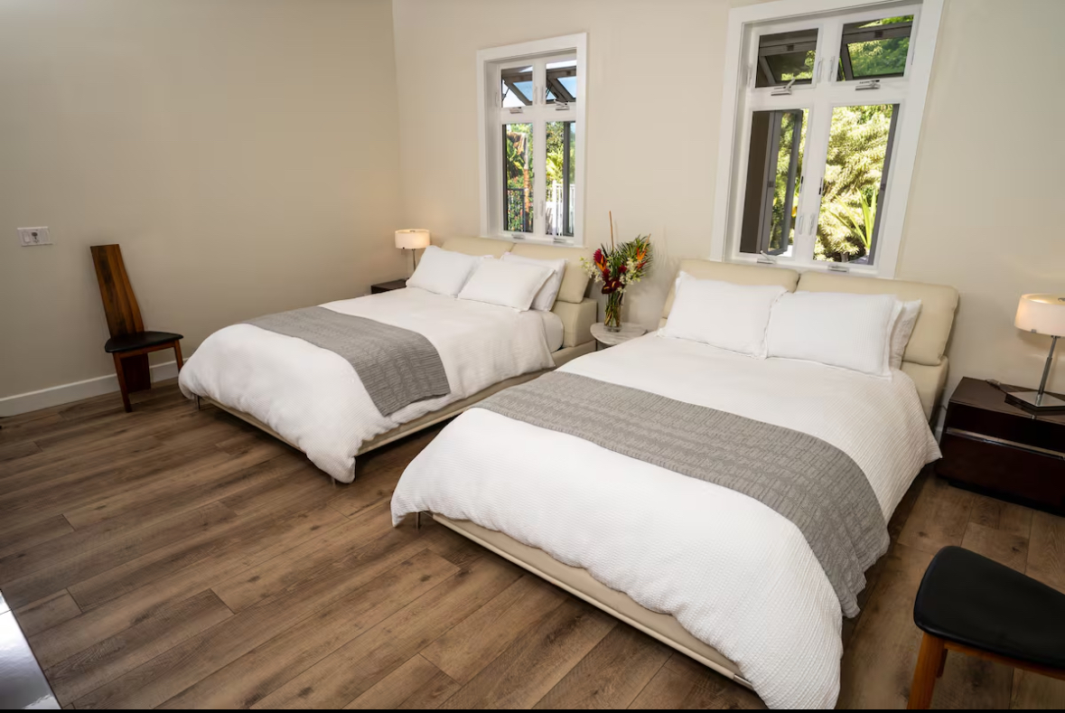 Bedroom with two beds and tall windows looking into tropical greenery