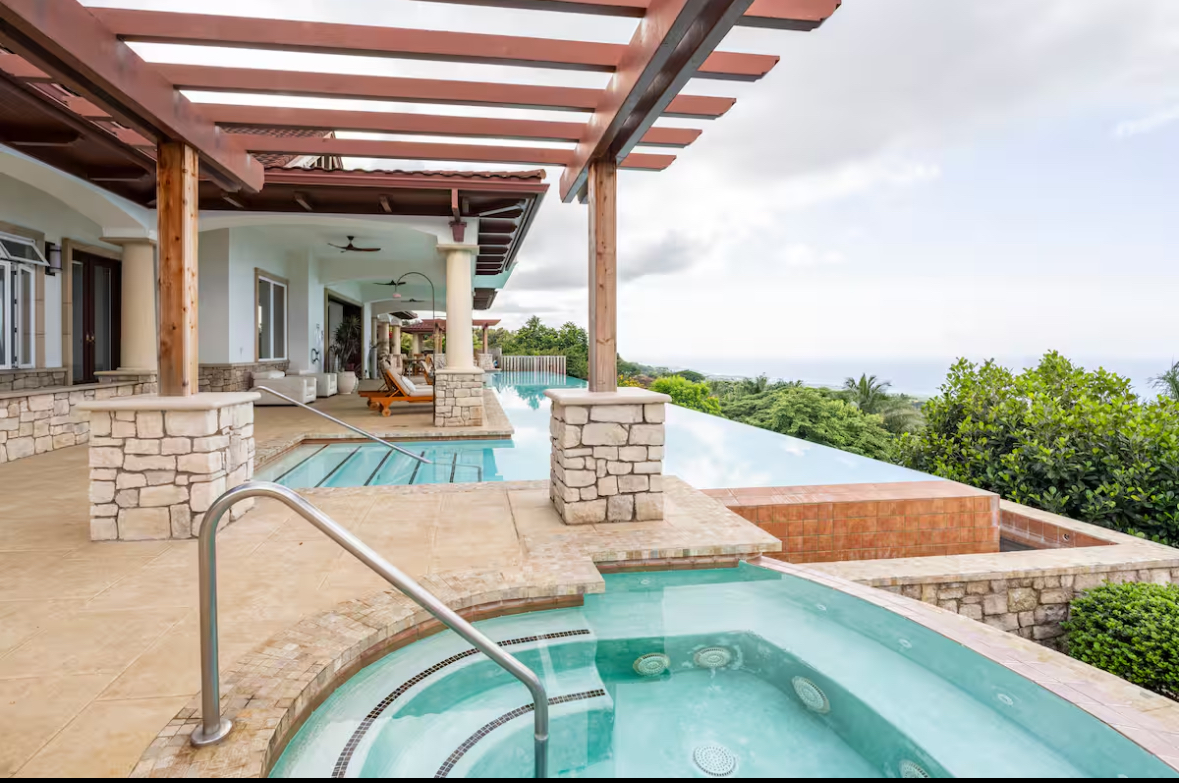 Infinity-edge pool and hot tub overlooking lush greenery and the ocean